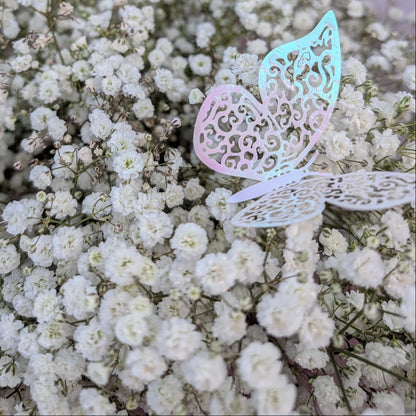 A close-up of a bouquet or floral arrangement made of dense white baby's breath flowers, with a pastel pink star-shaped balloon and a translucent iridescent butterfly decoration in the background.